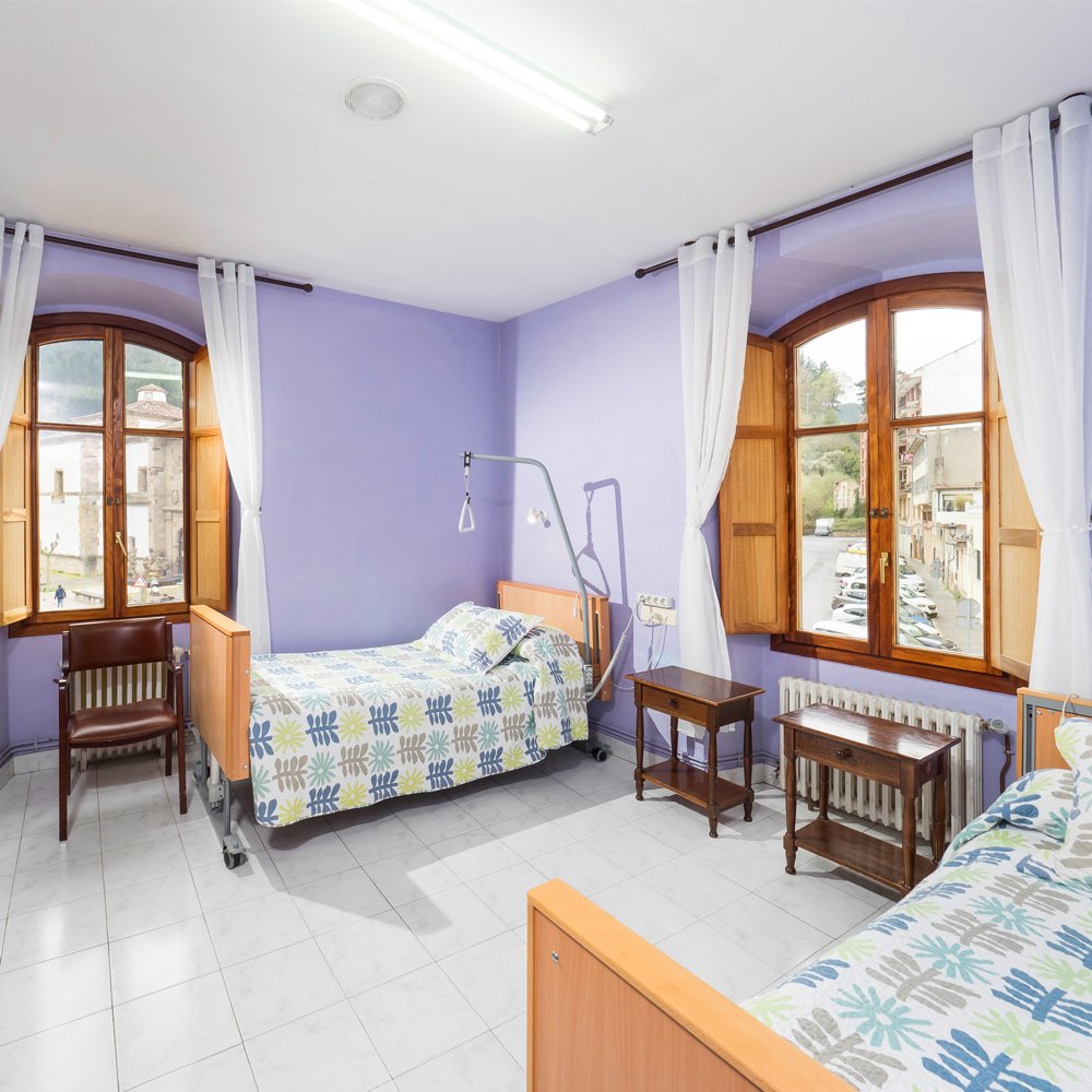 Vista de la habitación doble de la residencia de mayores León Trucíos con dos camas, mesillas de noche y sillas