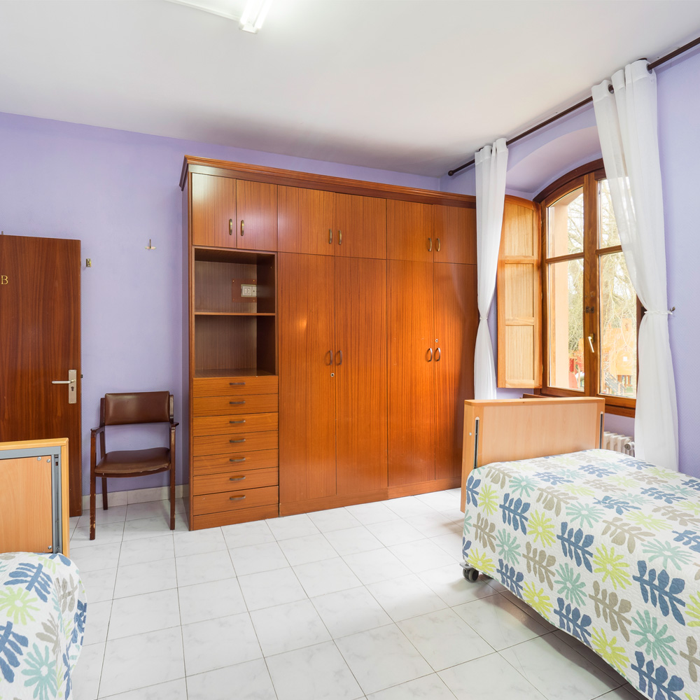 Vista de la habitación doble de la residencia de mayores León Trucíos con dos camas, sillas y armarios