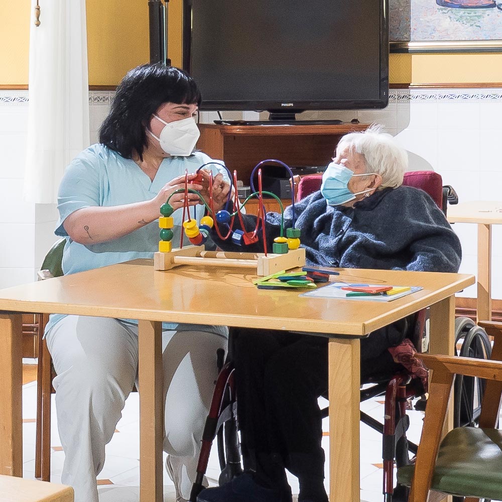 Una trabajadora de la residencia ayuda en un taller a una de las usuarias del centro de mayores